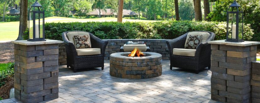 A beautiful outdoors pavers with two comfortable armchairs and a fire pit in a natural green environment